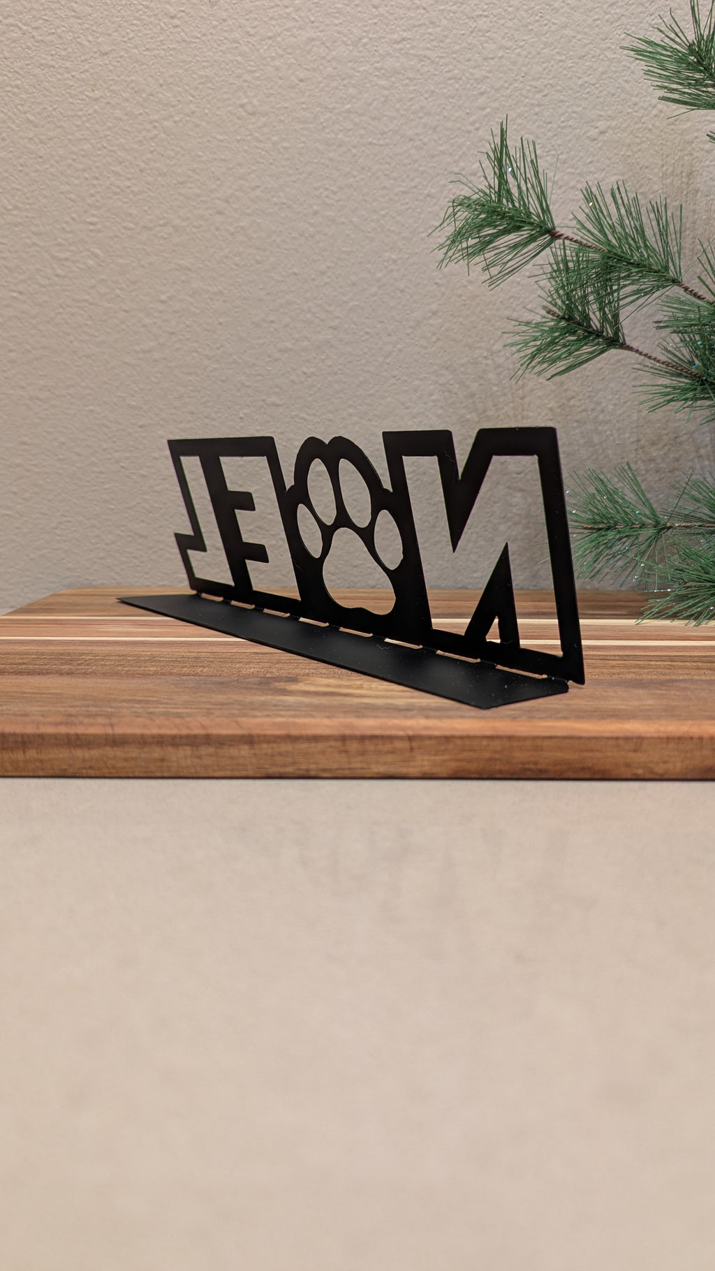 Rear quarter profile Image of a  black metal sign with the word "NOEL" and a paw for the "o" from Atomic Rat Rods & Metal Werks.
