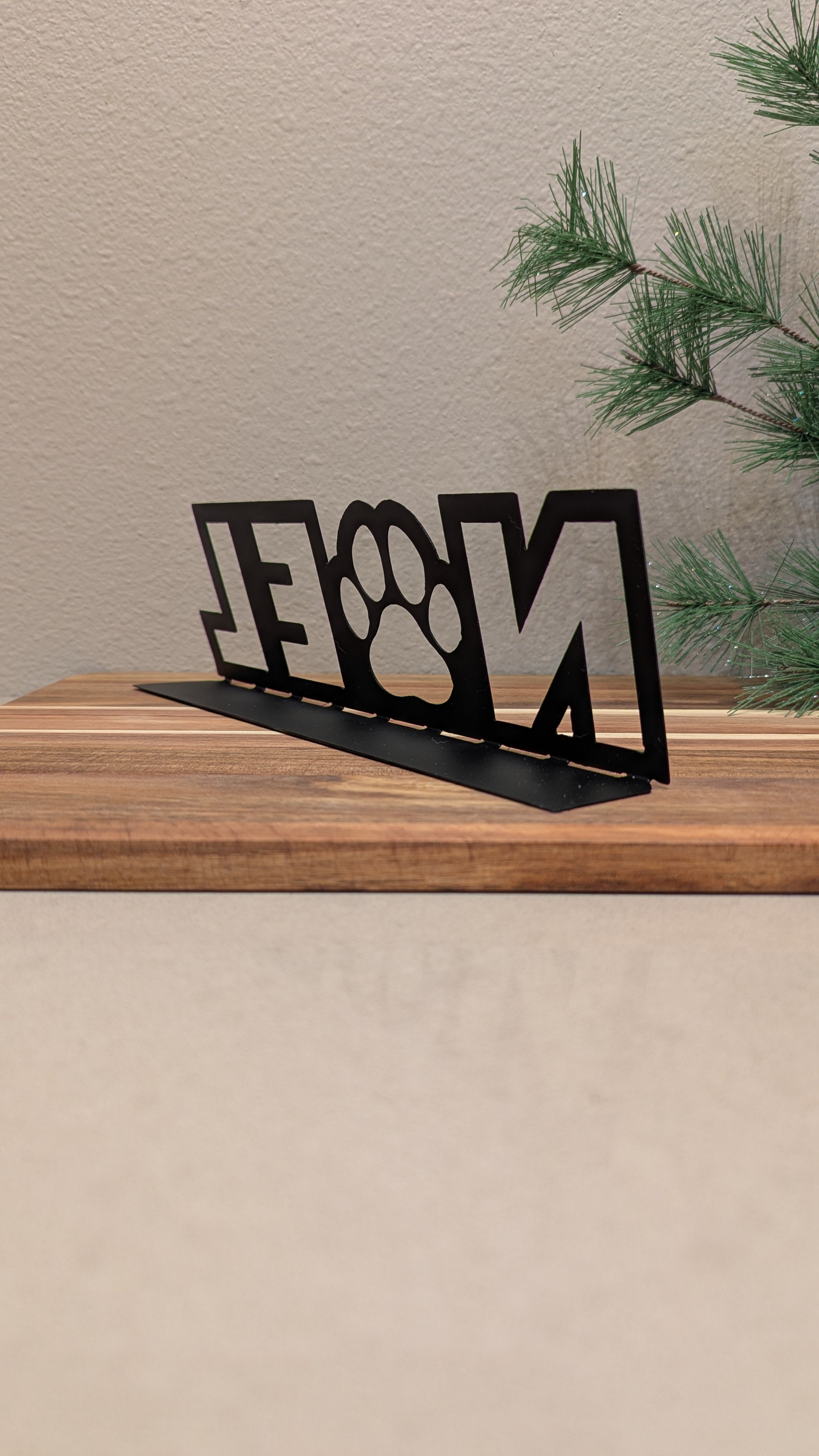 Rear quarter profile Image of a  black metal sign with the word "NOEL" and a paw for the "o" from Atomic Rat Rods & Metal Werks.