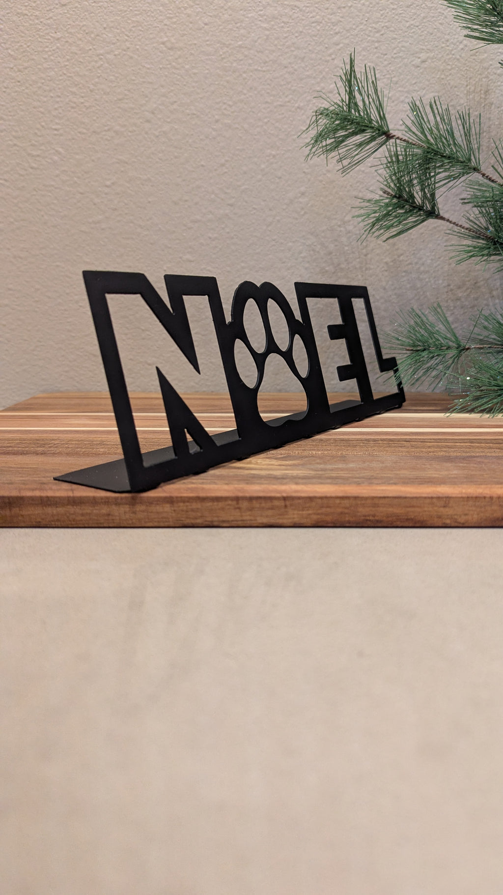 Front quarter Image of a  black metal sign of the word "NOEL" and a paw for the "o" from Atomic Rat Rods & Metal Werks.