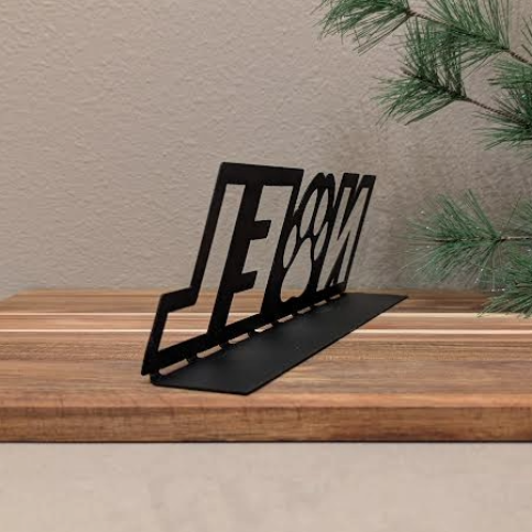 Opposite rear quarter view Image of a black metal sign with the word "NOEL" and a paw for the "o" from Atomic Rat Rods & Metal Werks. Christmas decorations in the background.