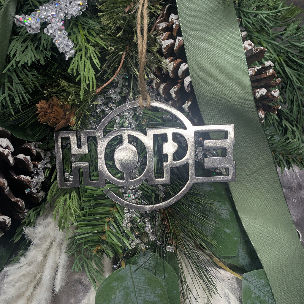 Panned out image of a simple, minimalist silver-colored "HOPE" ornament on a Christmas tree from Atomic Rat Rods & Metal Werks.