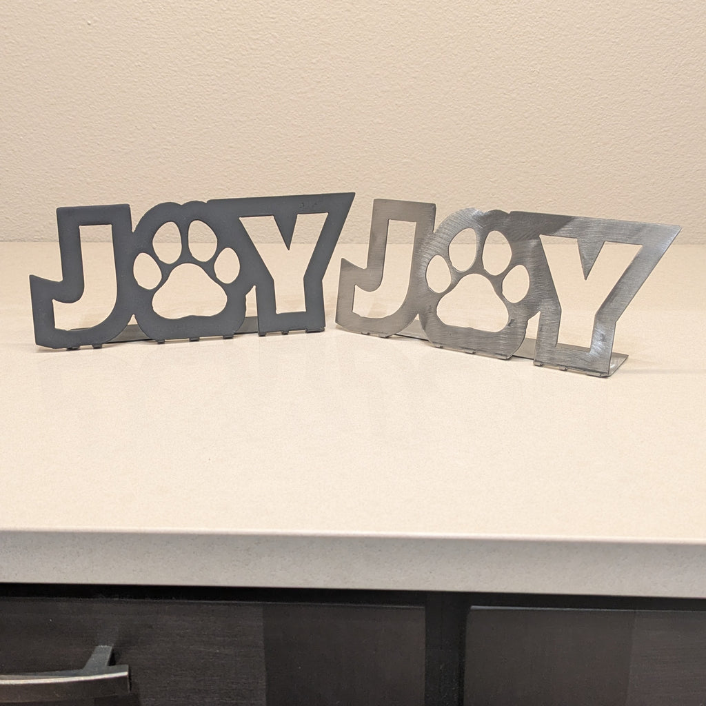 Image of side-by-side black and silver-colored metal signs with the word "JOY" and a paw for the "o" from Atomic Rat Rods & Metal Werks.