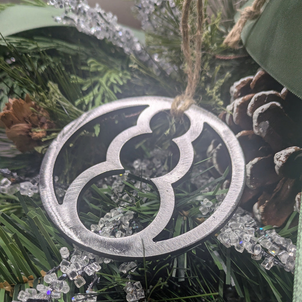 Angle image of a simple, minimalist silver-colored snowman ornament on a Christmas tree from Atomic Rat Rods & Metal Werks.